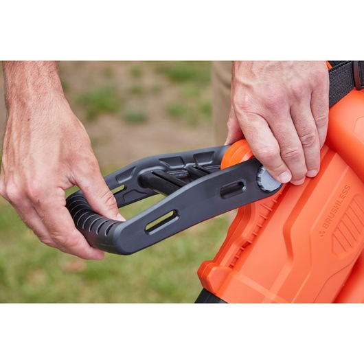 Close-up of hands adjusting BLACKDECKER BCBLV3625L1 orange leaf blower handle outdoors.