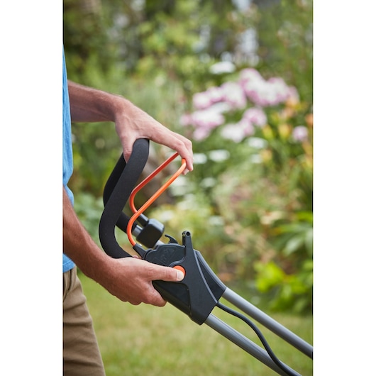 Photo of BLACKDECKER BCMW33184L2 lawn mower handle with orange control lever held by person outdoors.