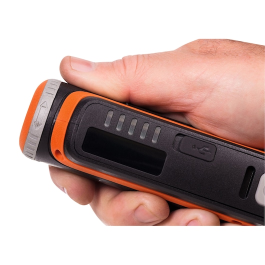 A close-up of a hand holding a BLACK+DECKER device with an orange and black exterior, featuring a display screen, indicator lights, and a USB port.