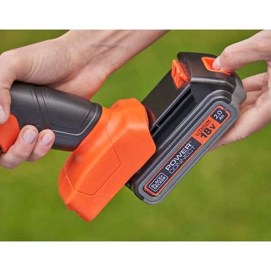 Close-up of a person installing a BLACK+DECKER POWERCONNECT 18V lithium battery pack into a cordless power tool, showing the orange and black handle and battery.