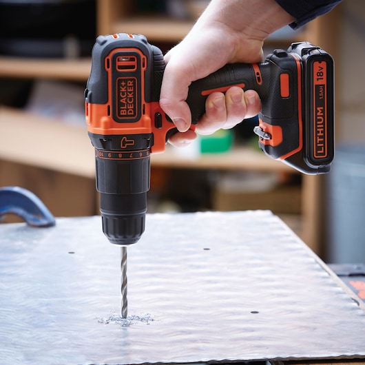 A person using a BLACK+DECKER 18V lithium cordless drill to drill into a sheet of metal.
