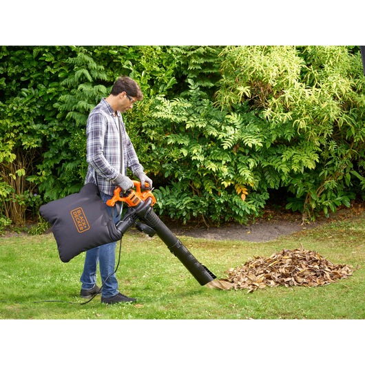 BLACKDECKER BEBLV260 leaf blower with collection bag in use outdoors near pile of dry leaves.