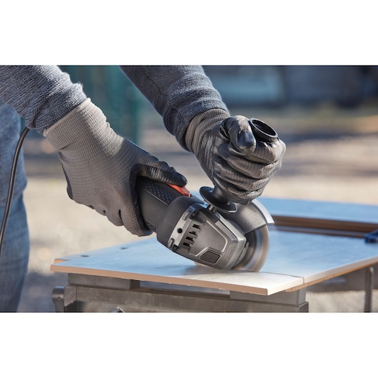 BLACKDECKER BEG120 angle grinder in use, cutting tile outdoors, close-up on gloved hands and tool.