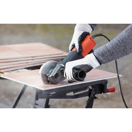 BLACKDECKER BEG120 angle grinder cutting tile, held by gloved hands outdoors, close-up photo.