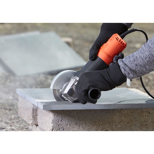 BLACKDECKER BEG120 angle grinder in use cutting stone, close-up of tool held by gloved hands.