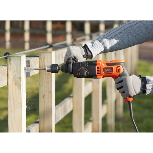 BLACKDECKER BEHS01 corded hammer drill in use, drilling wood outdoors with gloved hands.