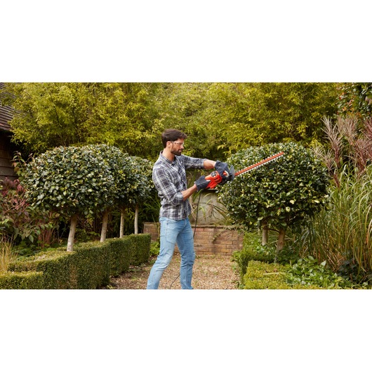 BLACKDECKER BEHT251 hedge trimmer held by person trimming bushes in a garden.