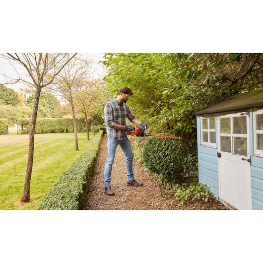 BLACKDECKER BEHTS501 hedge trimmer used outdoors near garden shed and shrubbery.