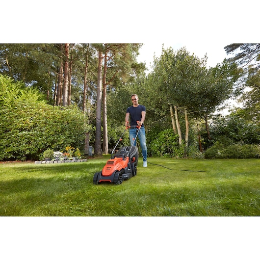 BLACKDECKER BEMW461BH lawn mower in use, orange body, user mowing grass in garden, outdoor scene.
