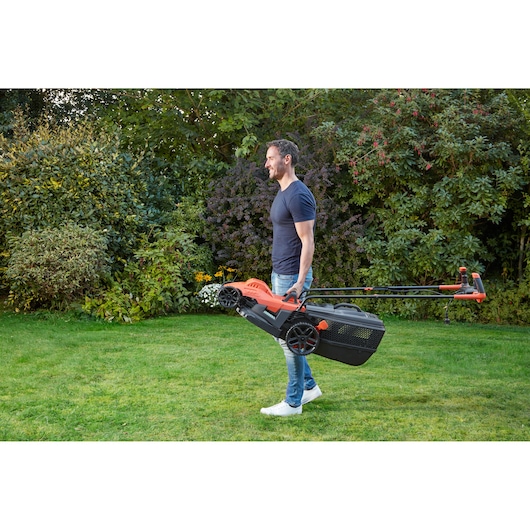 BLACKDECKER BEMW461BH lawn mower carried by person outdoors, orange and black design, garden setting.