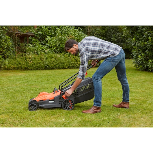 BLACKDECKER BEMW461BH lawn mower being adjusted outdoors on grass.