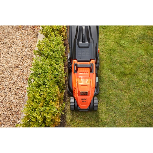 BLACK+DECKER BEMW461BH lawn mower top view cutting grass along hedge.