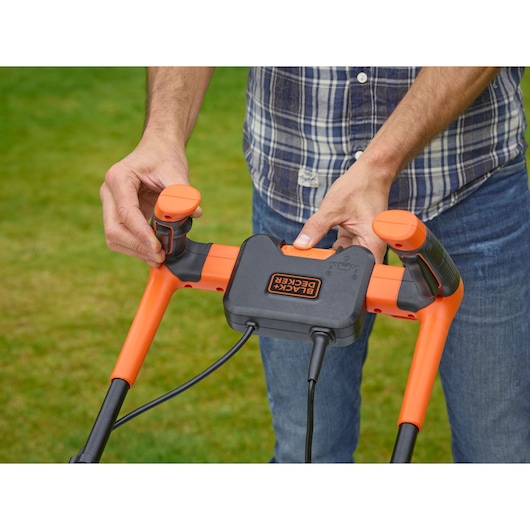 Photo of BLACKDECKER BEMW461BH lawn mower handle with orange controls and visible cable outdoors.