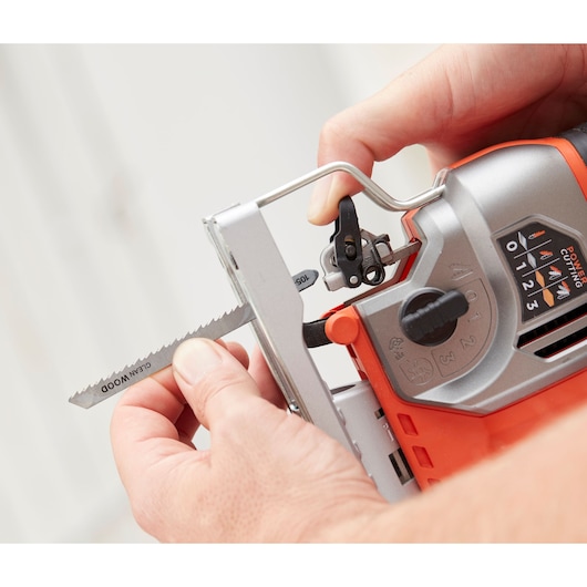 Close-up of hands inserting a saw blade into a BLACK+DECKER jigsaw, model BES610, with visible control panel and settings.