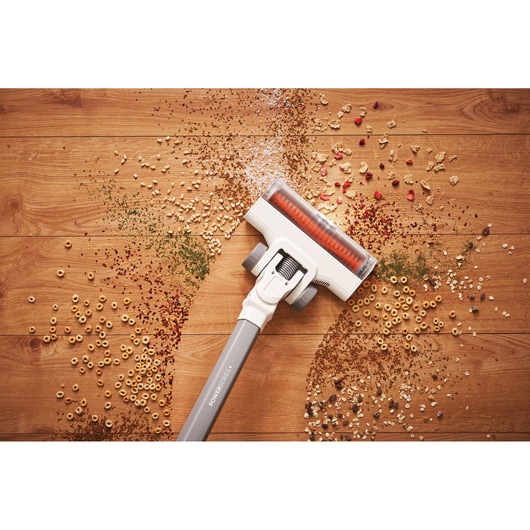 A cordless vacuum cleaner head cleaning assorted dry debris and cereal from a wooden floor.