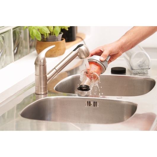A person rinses a vacuum filter under running water in a kitchen sink with a stainless steel faucet.