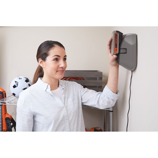 Person placing BLACKDECKER BHFEV182C battery into wall-mounted charger in a garage or storage area.