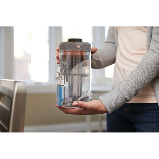 Photo of a person holding a BLACKDECKER BHFEV362D vacuum dust canister in a home setting.