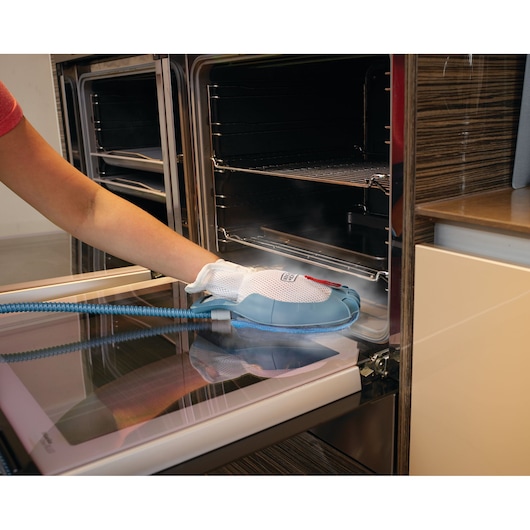 A person is cleaning the inside of an open oven with a BLACK+DECKER steam cleaning glove attachment.