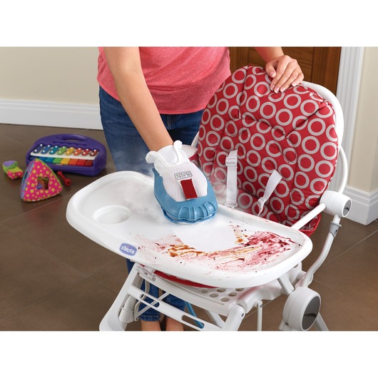 A person is using a BLACK+DECKER steam cleaning glove to clean the tray of a red and white high chair with visible food stains. Children's toys, including a colorful keyboard, are on the floor in the background.