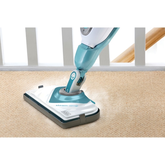 A BLACK+DECKER steam mop is shown cleaning a carpeted floor beside a white railing.