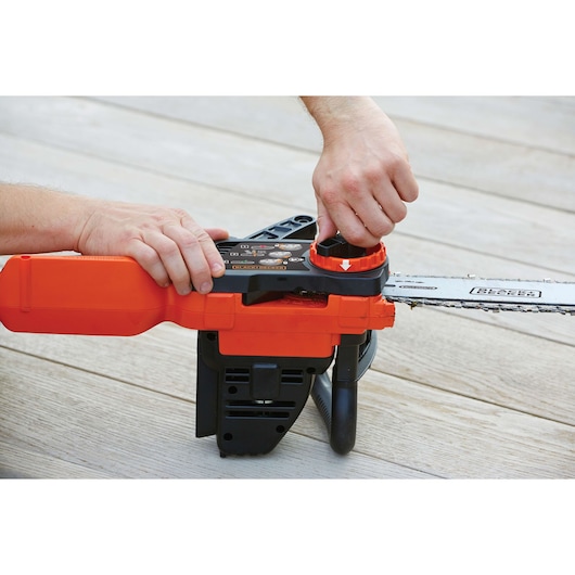 A person adjusting the chain tension on an orange and black BLACK+DECKER cordless chainsaw placed on a wooden surface.