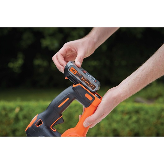 A close-up of hands inserting an 18V lithium battery into a BLACK+DECKER cordless power tool outdoors.