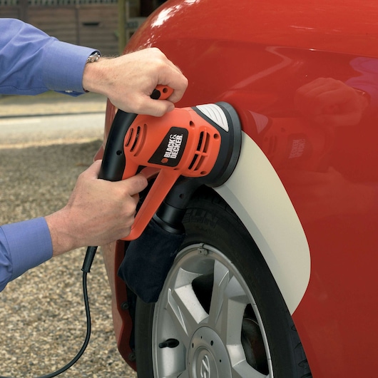 A person uses a BLACK+DECKER electric sander on the body of a red car, focusing on the area above the wheel.