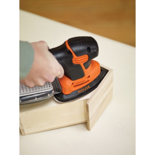 A person is using a BLACK+DECKER KA2500K Mouse sander to smooth the surface of a wooden box corner.
