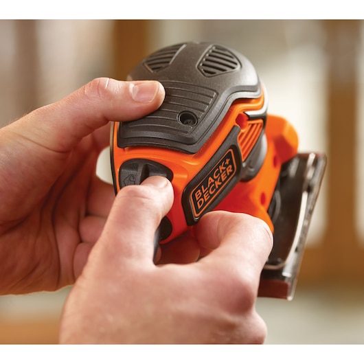Close-up of someone holding a BLACK+DECKER KA450 power sander, showing the details of the tool and the brand logo.