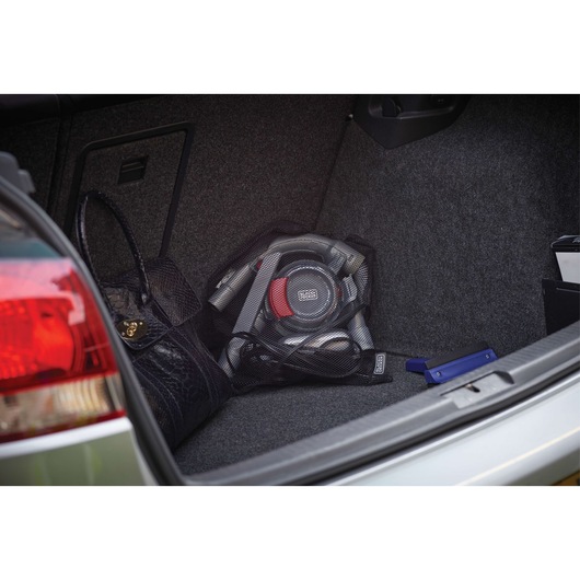A BLACK+DECKER portable car vacuum cleaner (model PD1200AV) placed in the trunk of a vehicle, next to a black handbag and other items.