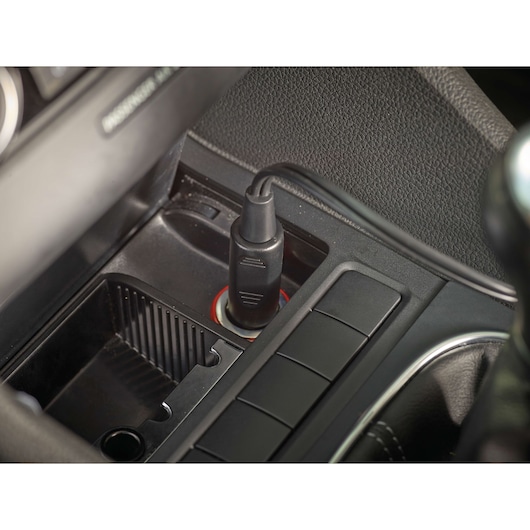 A close-up view of a Black+Decker car accessory plugged into a vehicle's 12V socket, located in the center console area.