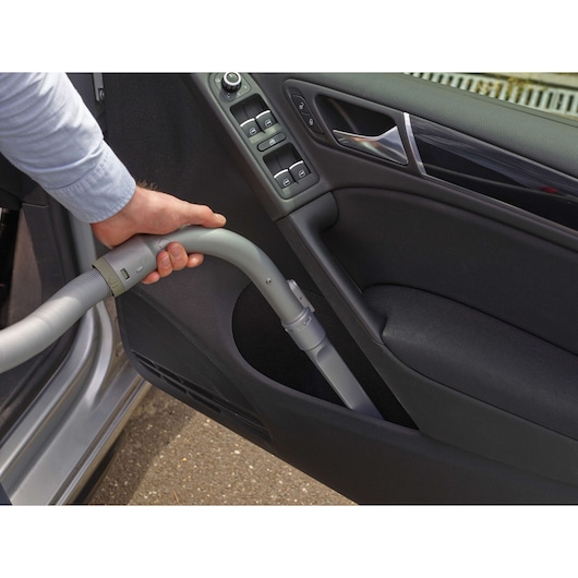 A hand using a vacuum cleaner with a flexible hose to clean the interior door panel of a car.